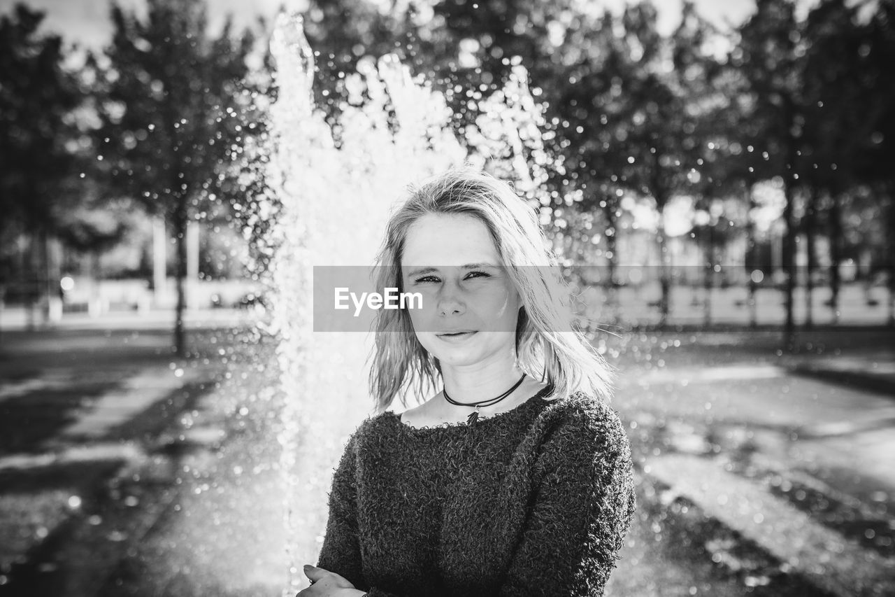 Portrait of young woman standing against fountain