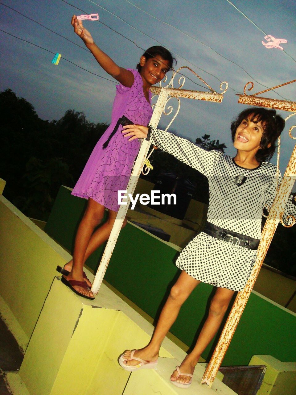 Full length of playful girls standing on retaining wall against cloudy sky at dusk