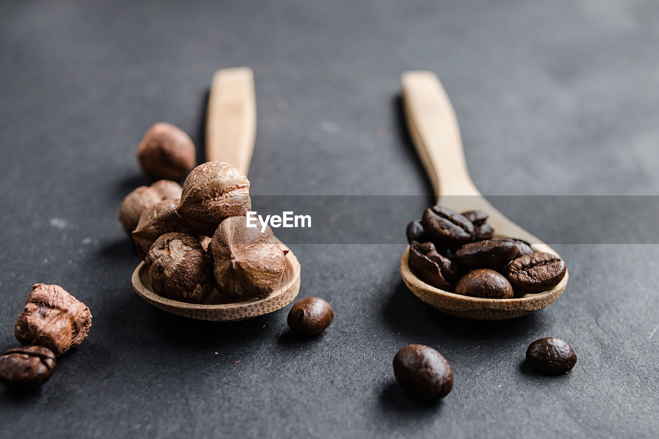 Close-up of hazelnuts with roasted coffee beans in wooden spoons on table