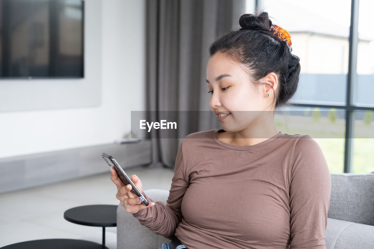 Young woman using phone while sitting on sofa at home