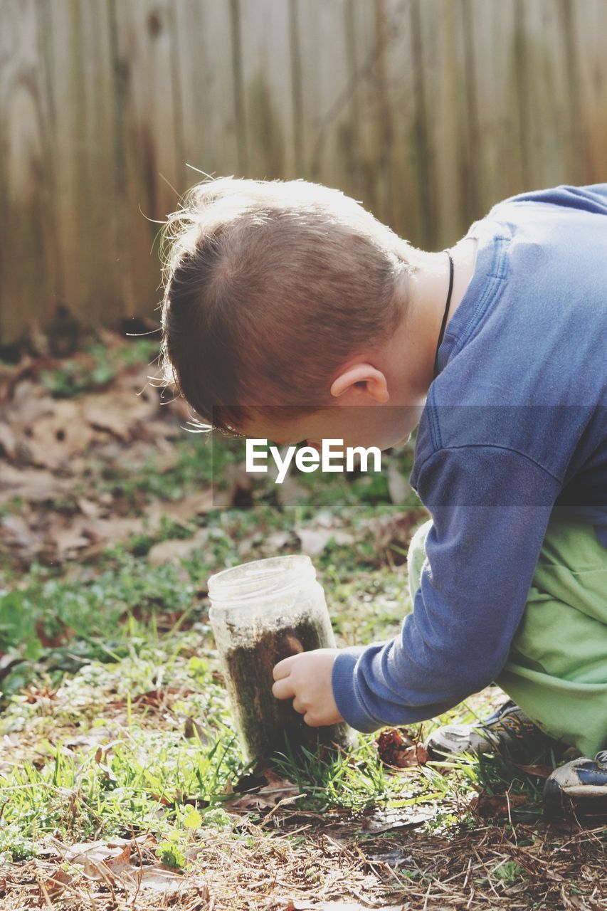 Boy looking at dirt in container on grass