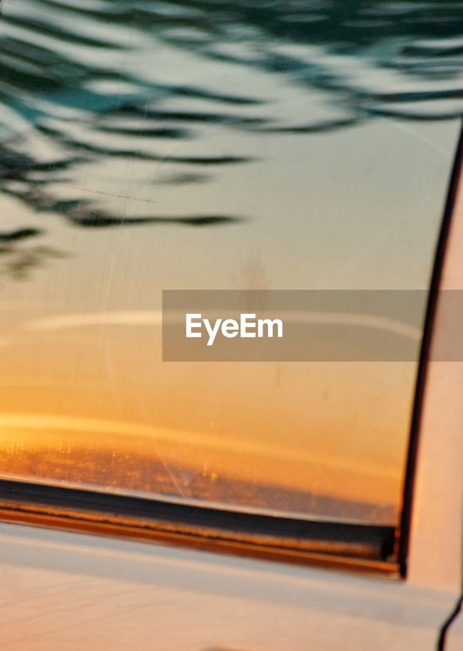 CLOSE-UP OF GLASS WINDOW AGAINST SUNSET SKY