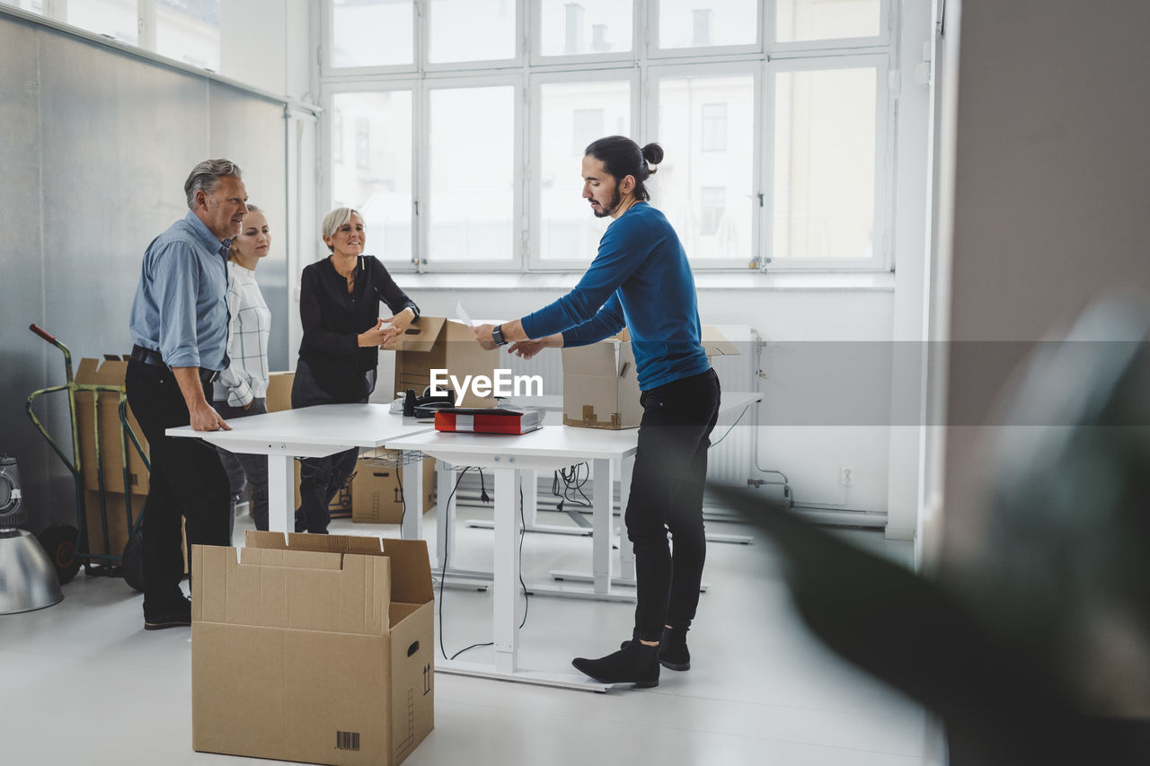 Multi-ethnic male and female business people unpacking cardboard boxes in new office