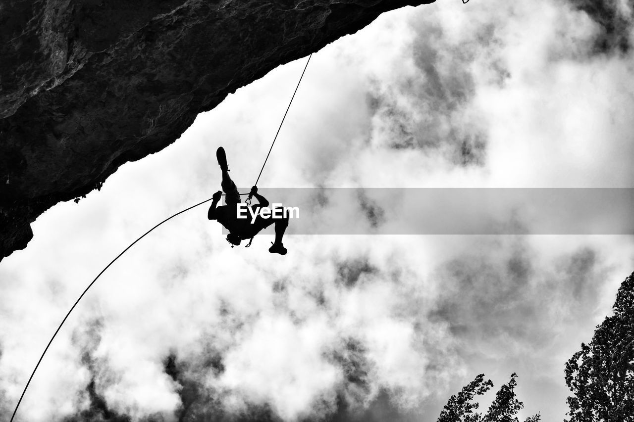 Low angle view of man hanging from rope by mountain