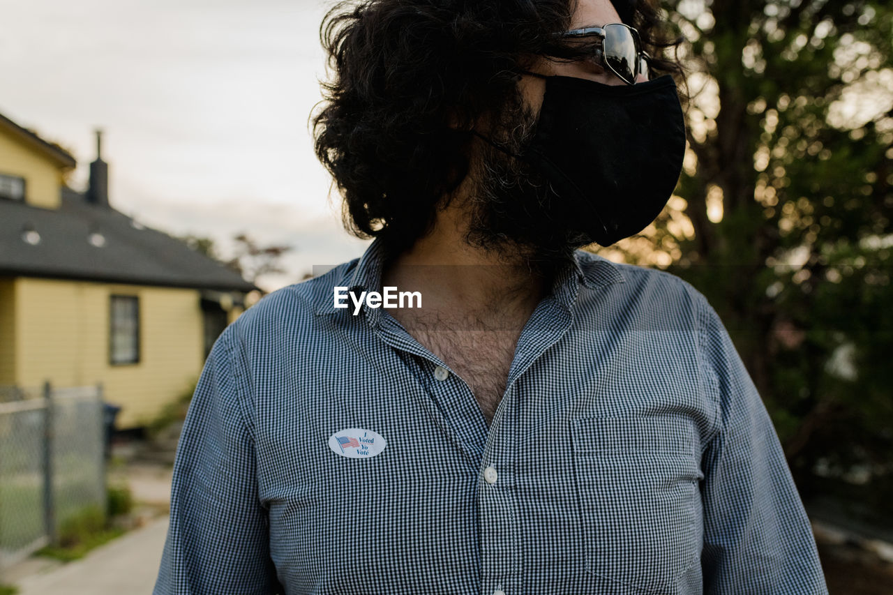 Man wearing face mask and sunglasses with 'i voted by mail' sticker