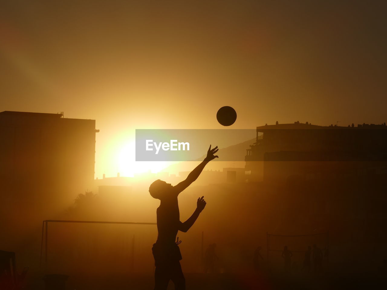 Side view of silhouette boy playing basketball at sunset