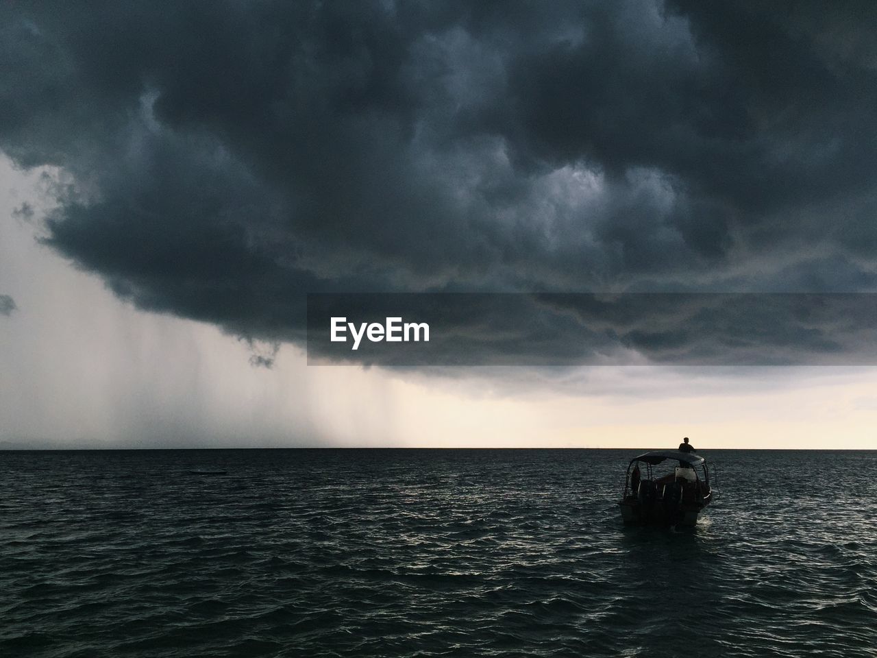 Man sailing boat in ocean against storm clouds