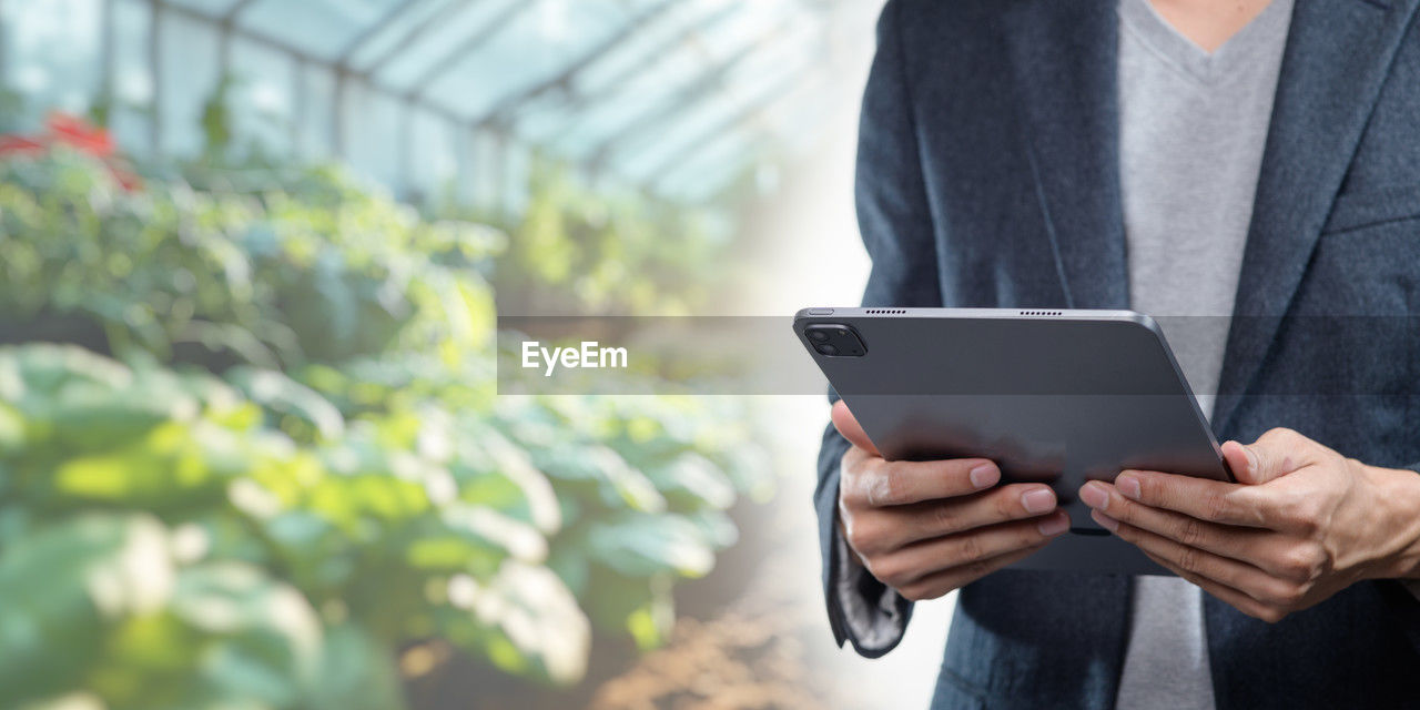 adult, technology, business, digital tablet, one person, communication, wireless technology, holding, greenhouse, standing, men, computer, business finance and industry, working, growth, occupation, portability, indoors, midsection, day, internet, plant nursery, convenience, nature, agriculture, front view, computer network, using computer, copy space, businessman, clothing, plant, mature adult, focus on foreground, flower, small business, botany, spring