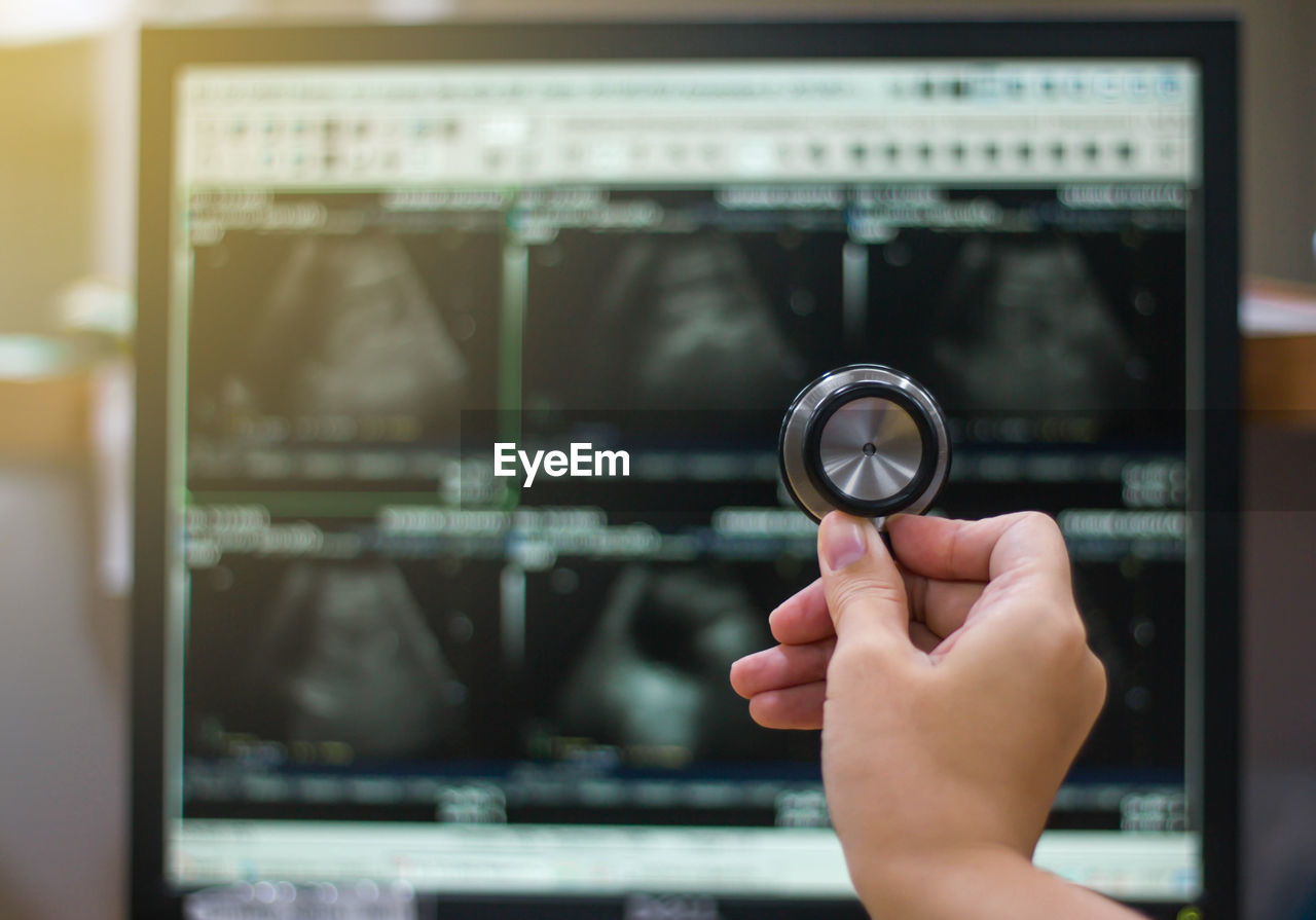 Cropped hand of doctor holding stethoscope against device screen