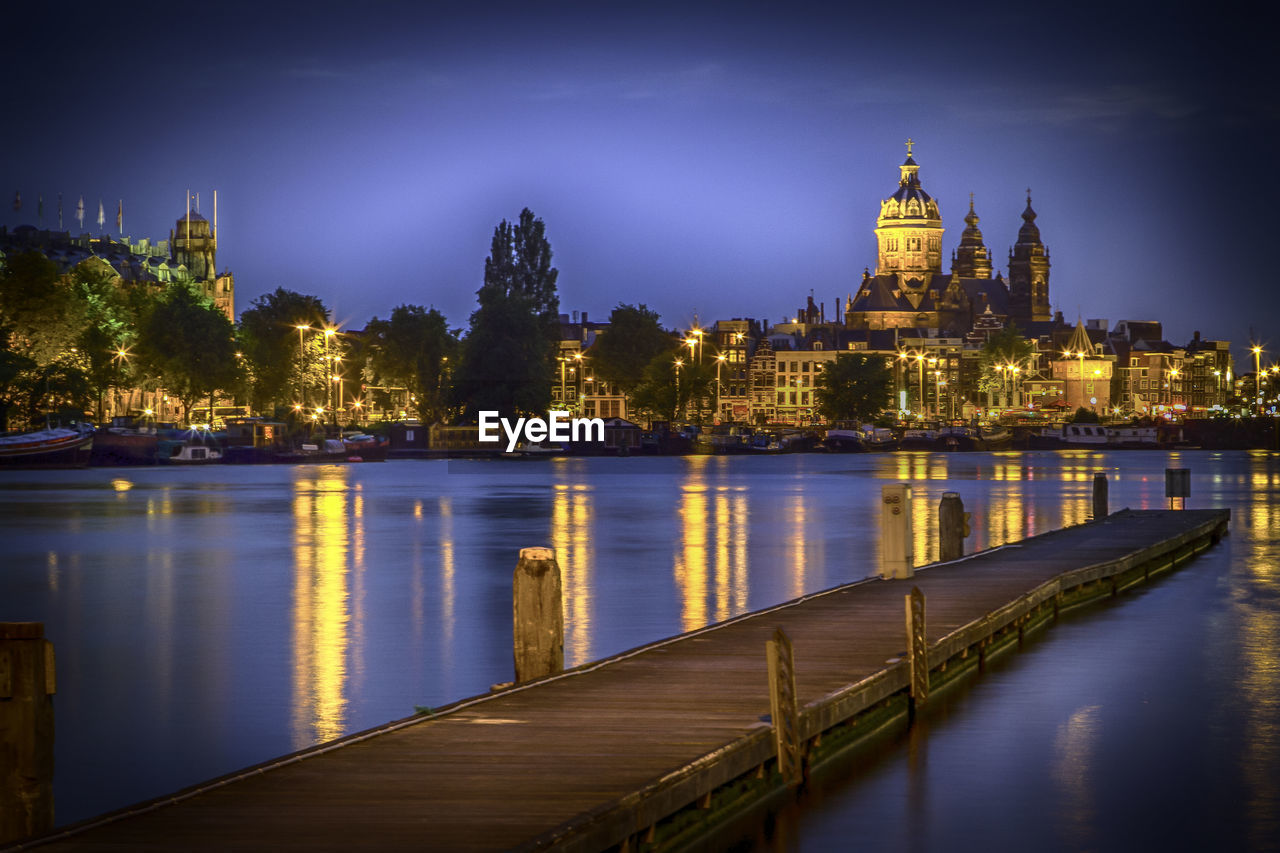 Illuminated building by river against sky at night