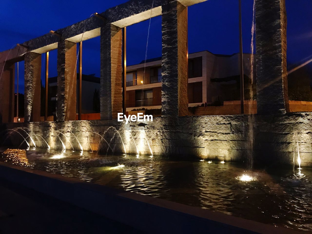 Illuminated bridge over river by buildings against sky at night