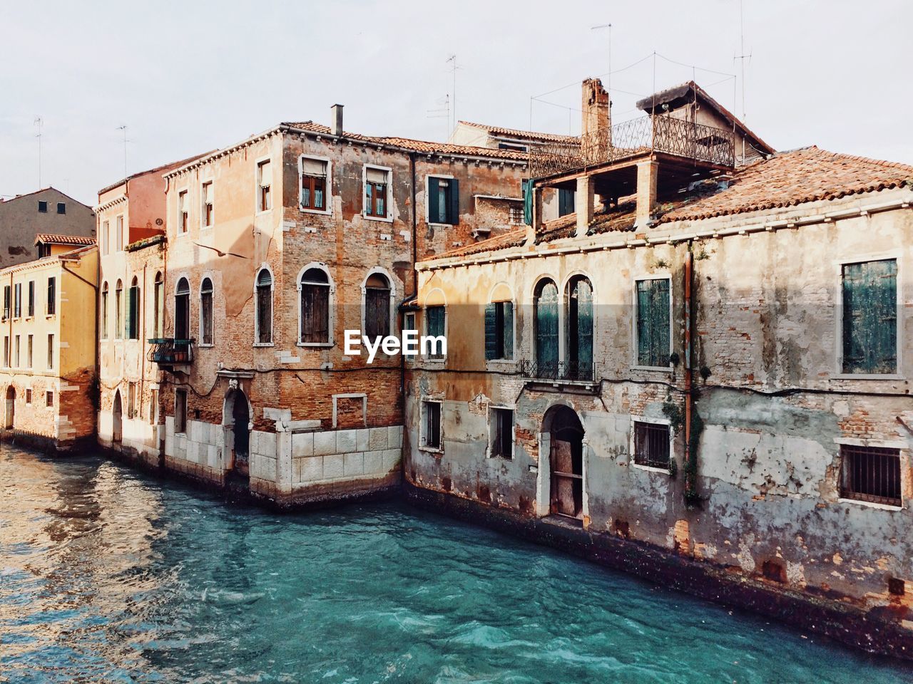 Canal by old buildings against sky