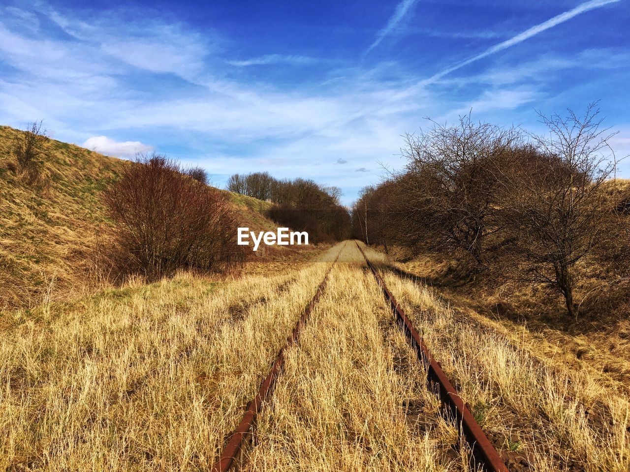 Railroad track on grassy field against blue sky