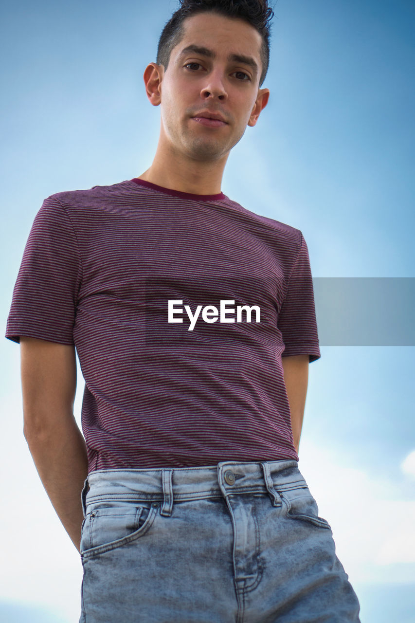 Low angle portrait of young man standing against sky