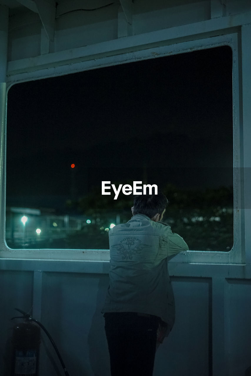 Rear view of woman standing by window at night