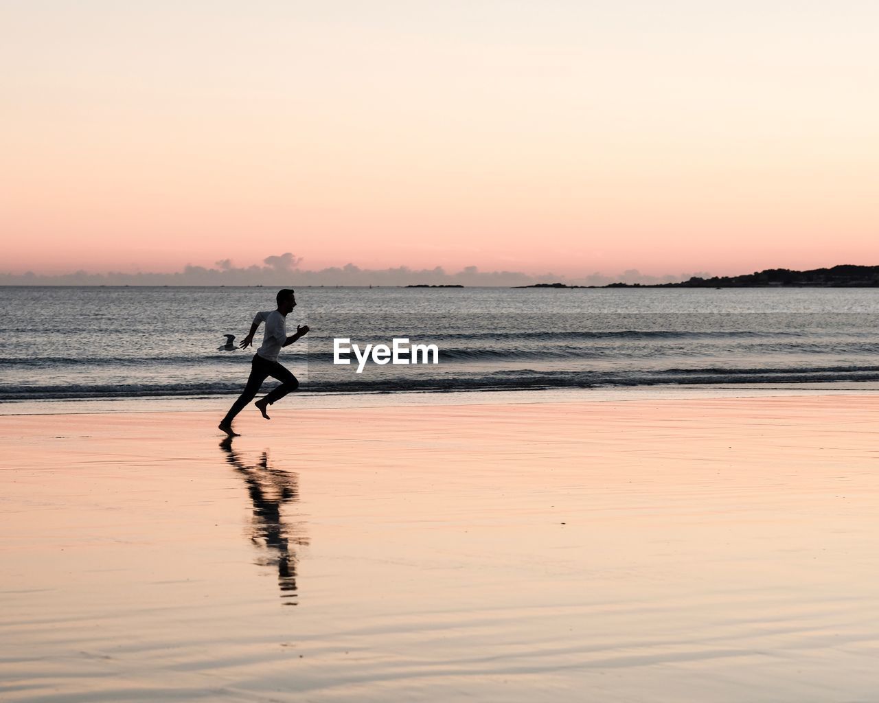 Side view of man running at beach against sky during sunset