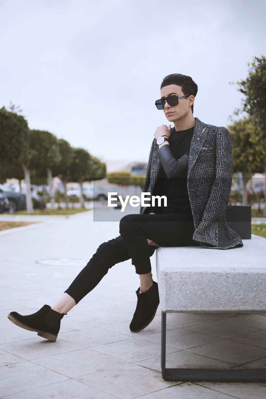 Full length of male model sitting on bench in city
