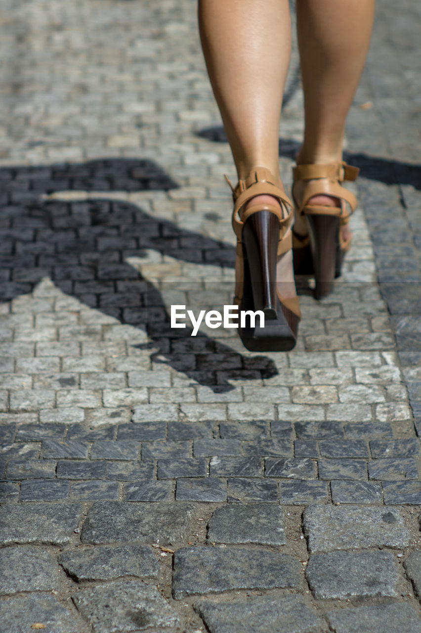 Low section of woman walking on cobble street