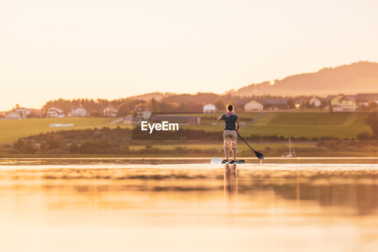 Young woman stand up paddling at sunset, lake wallersee, austria