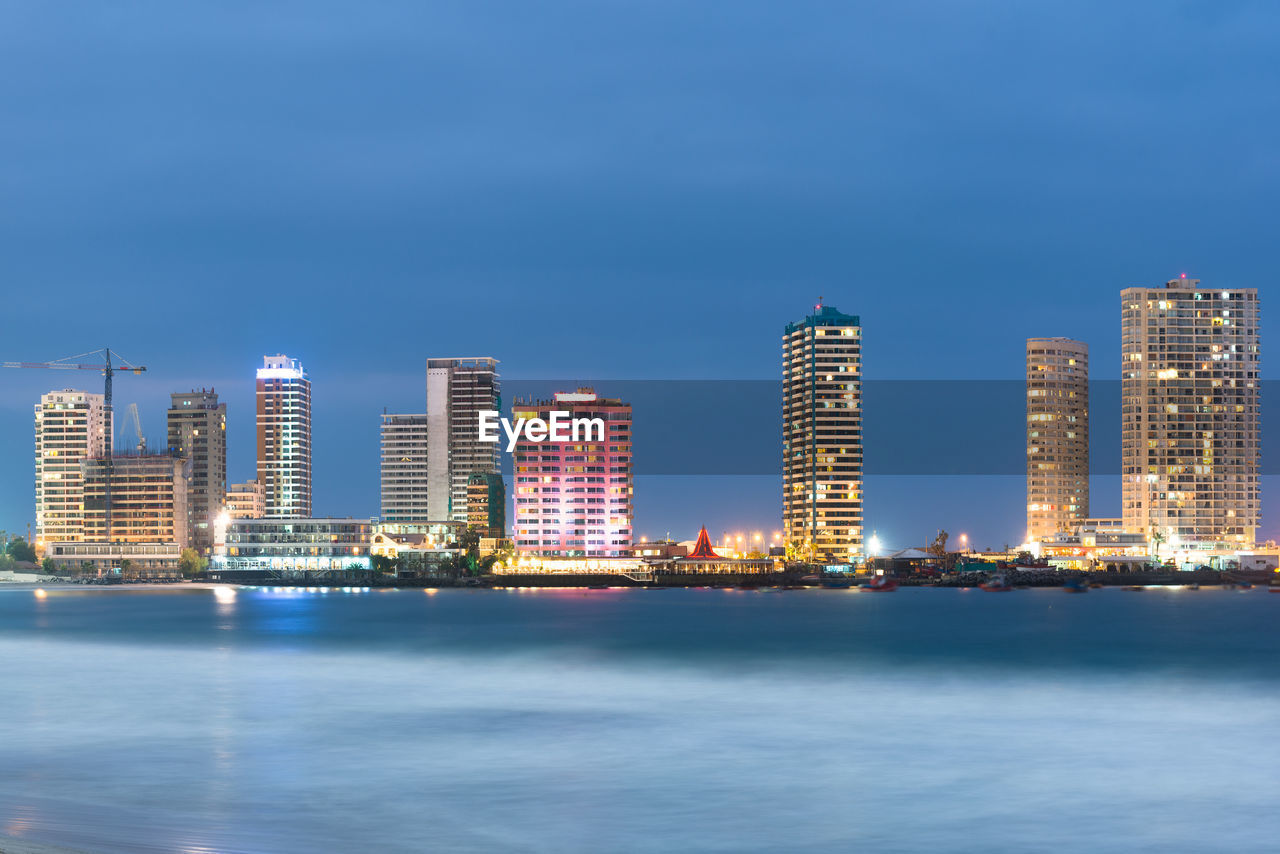 SEA BY ILLUMINATED CITY AGAINST BLUE SKY