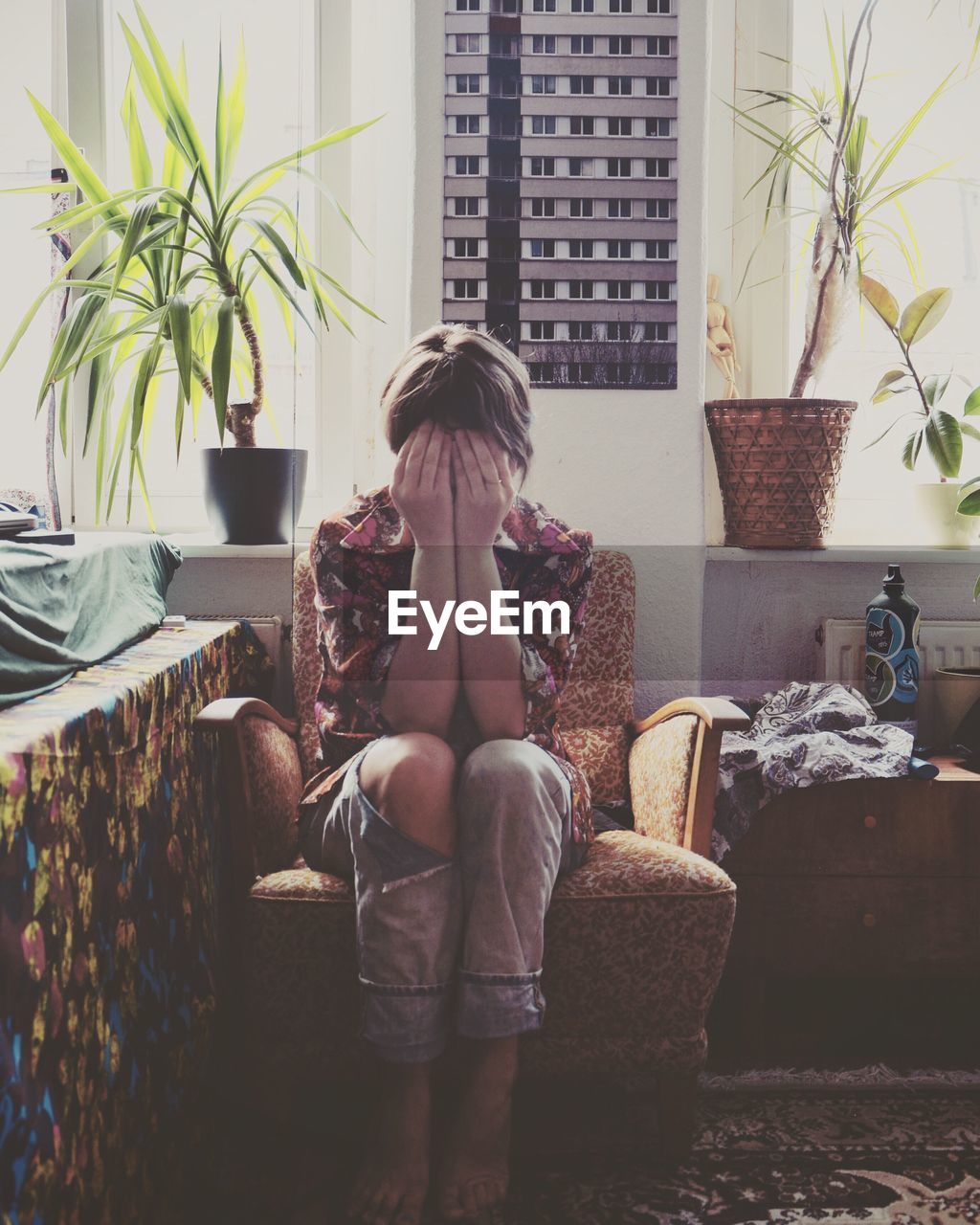 Woman covering face while sitting on chair at home