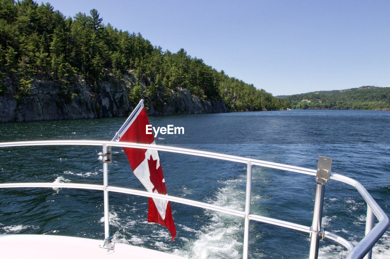 Boat sailing on lake against clear sky with canadian flag 