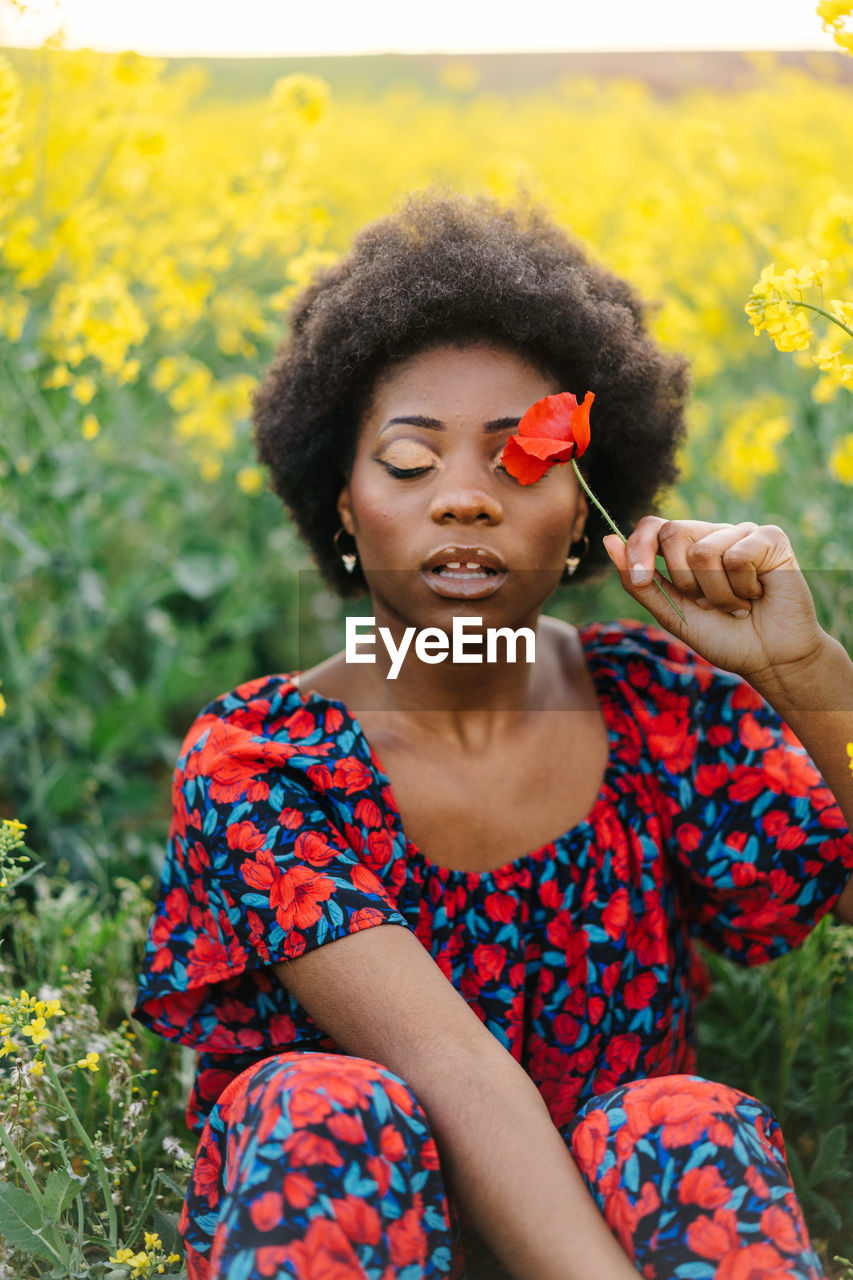 Close-up of young woman holding flower at field