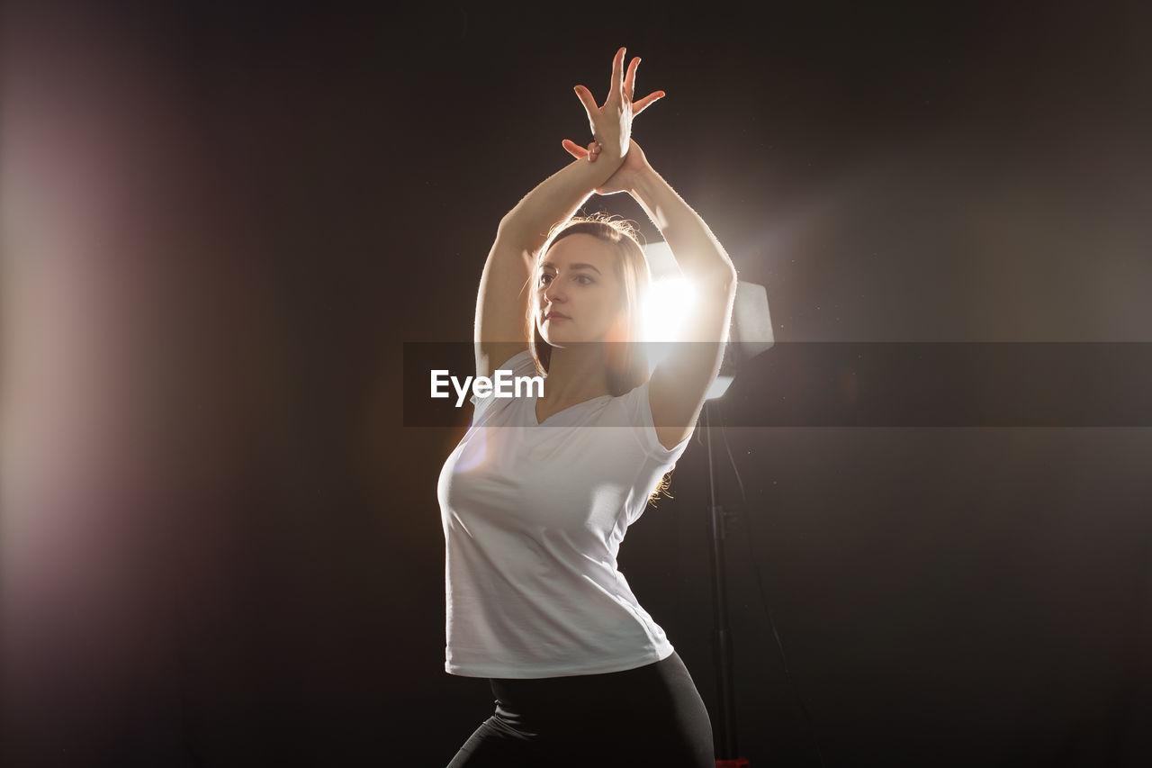 Young woman dancing at studio against black background