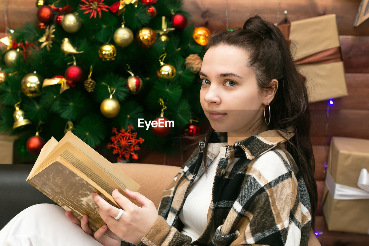 A young girl is reading a book comfortably sitting on the sofa on new year's eve.