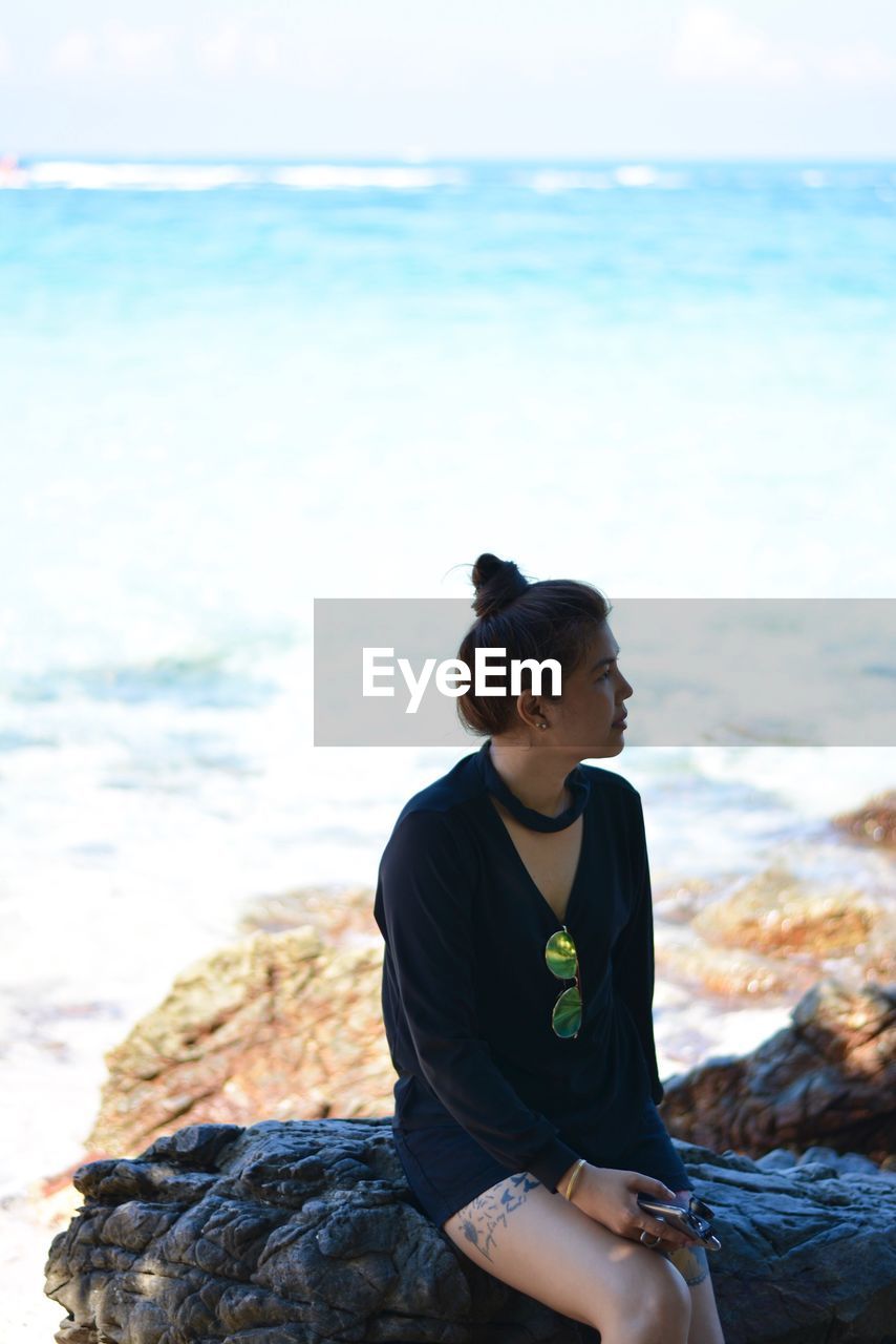 Woman sitting on rock by sea against sky