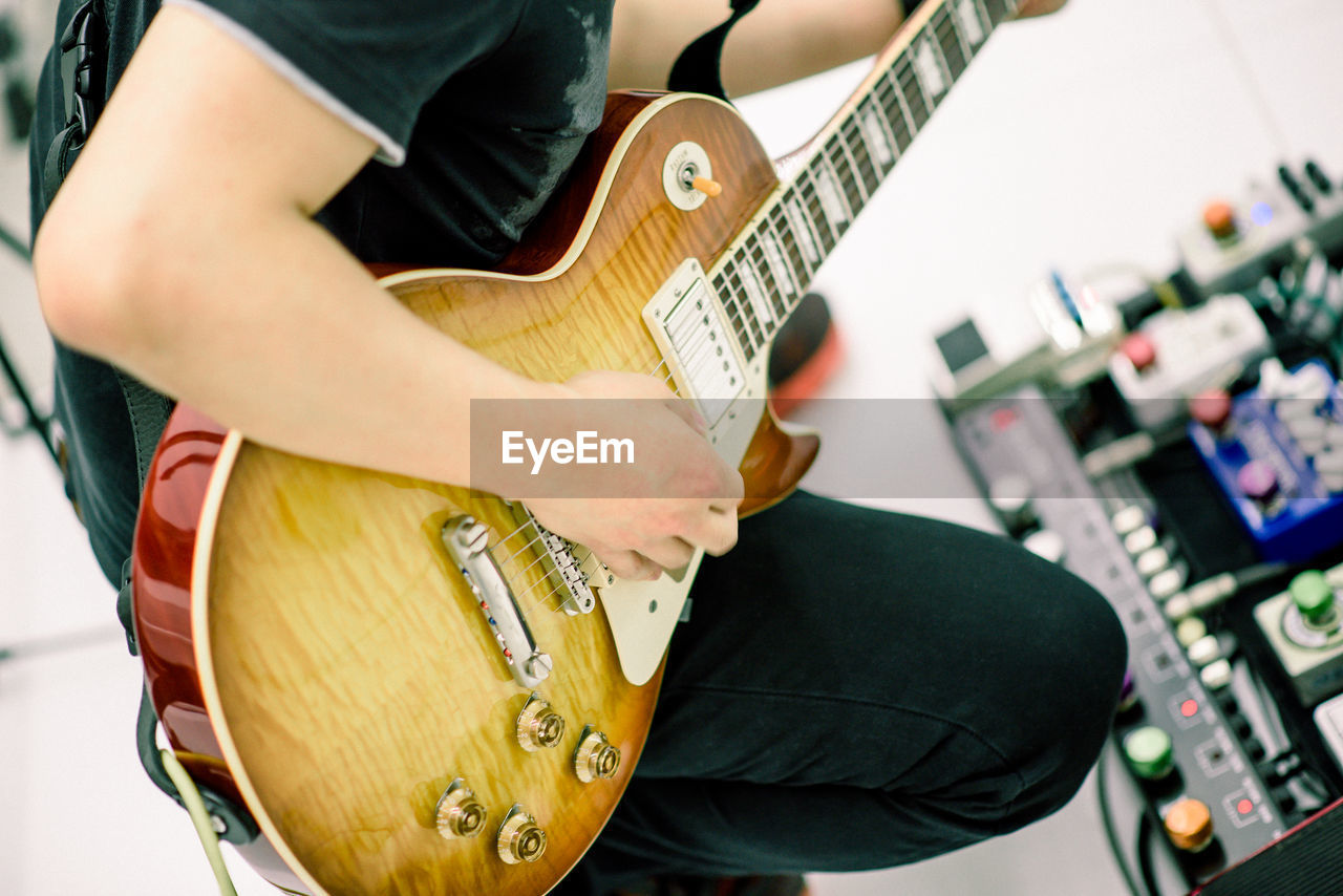 Midsection of man playing guitar at recording studio