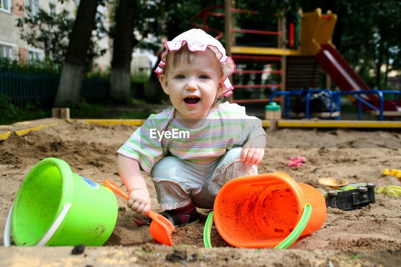 Portrait of cute happy girl playing with sand pail and shovel in sand