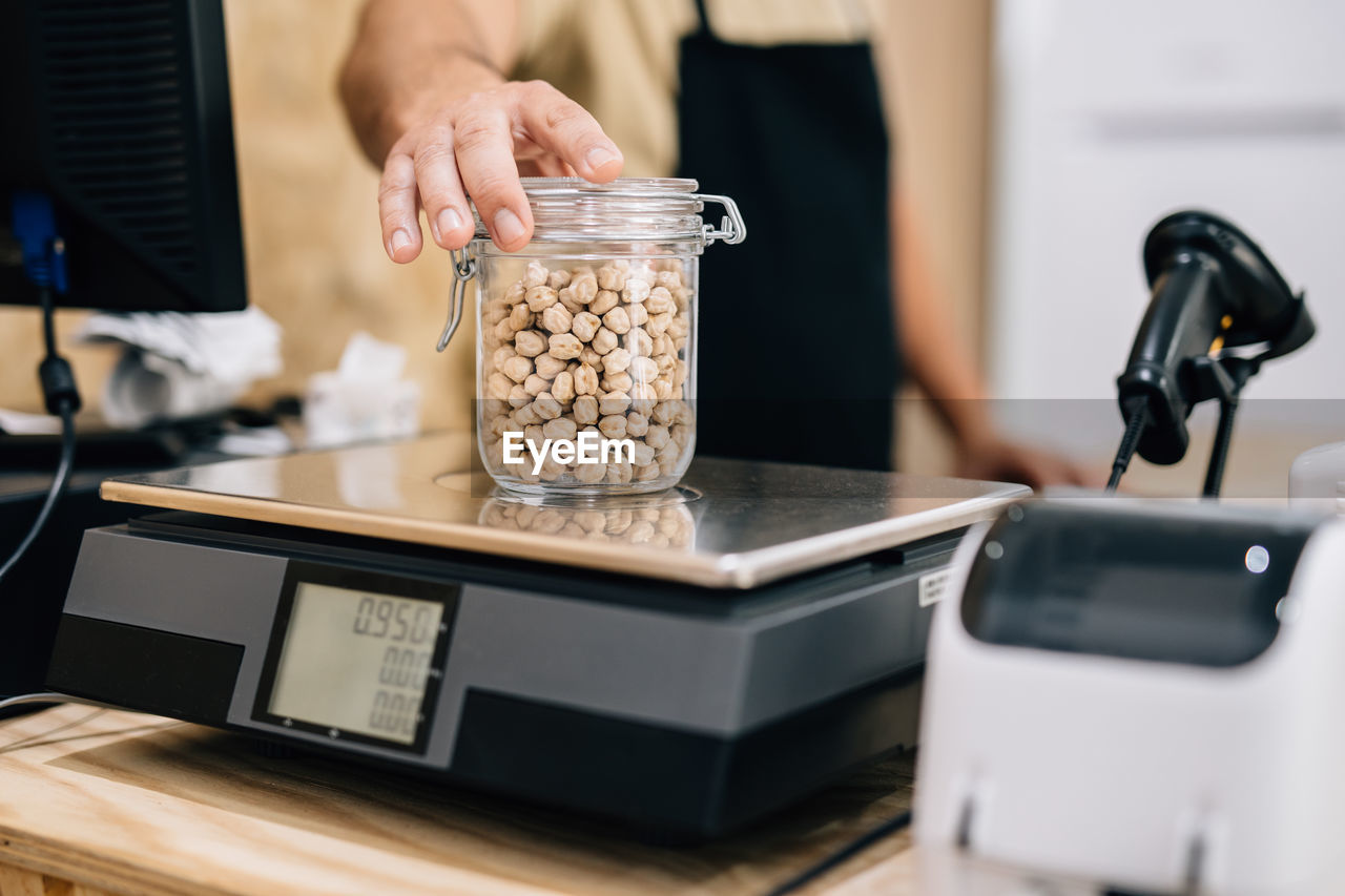 Anonymous shopkeeper checking weight of chickpeas on electronic scales