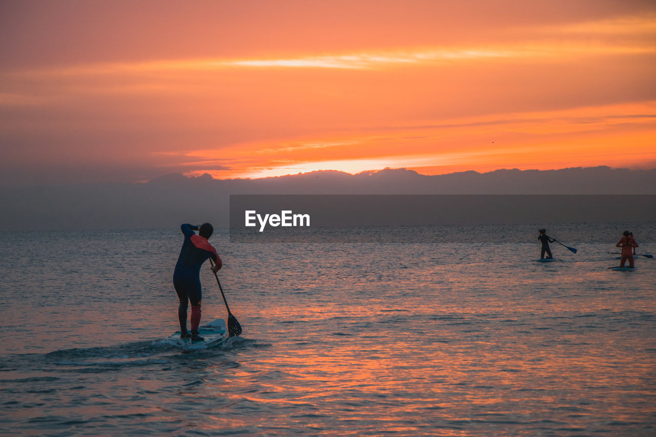 SILHOUETTE PEOPLE STANDING ON SEA AGAINST ORANGE SKY