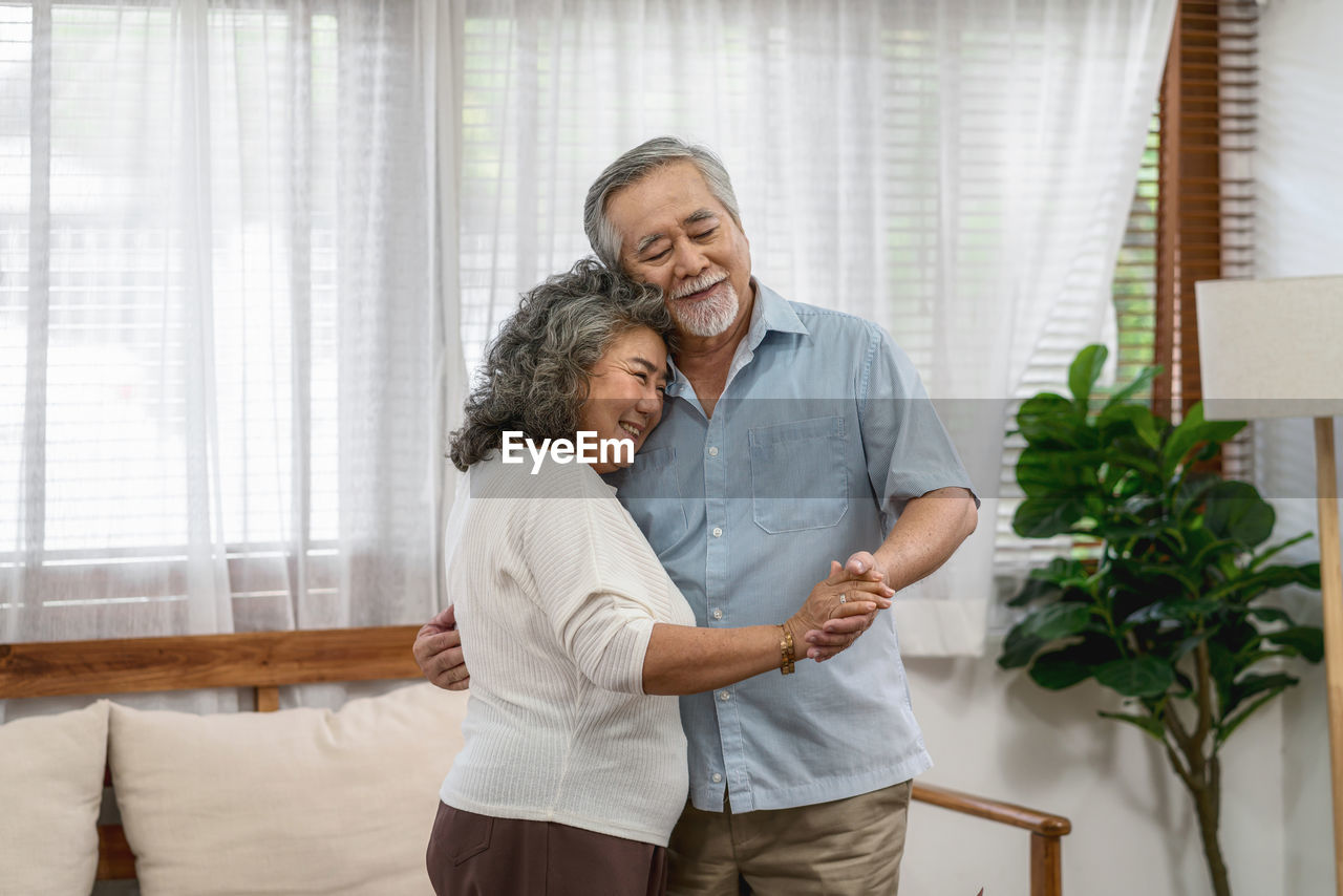 Asian couple grandparent dancing and hugging together with happy feeling in house, romantic 