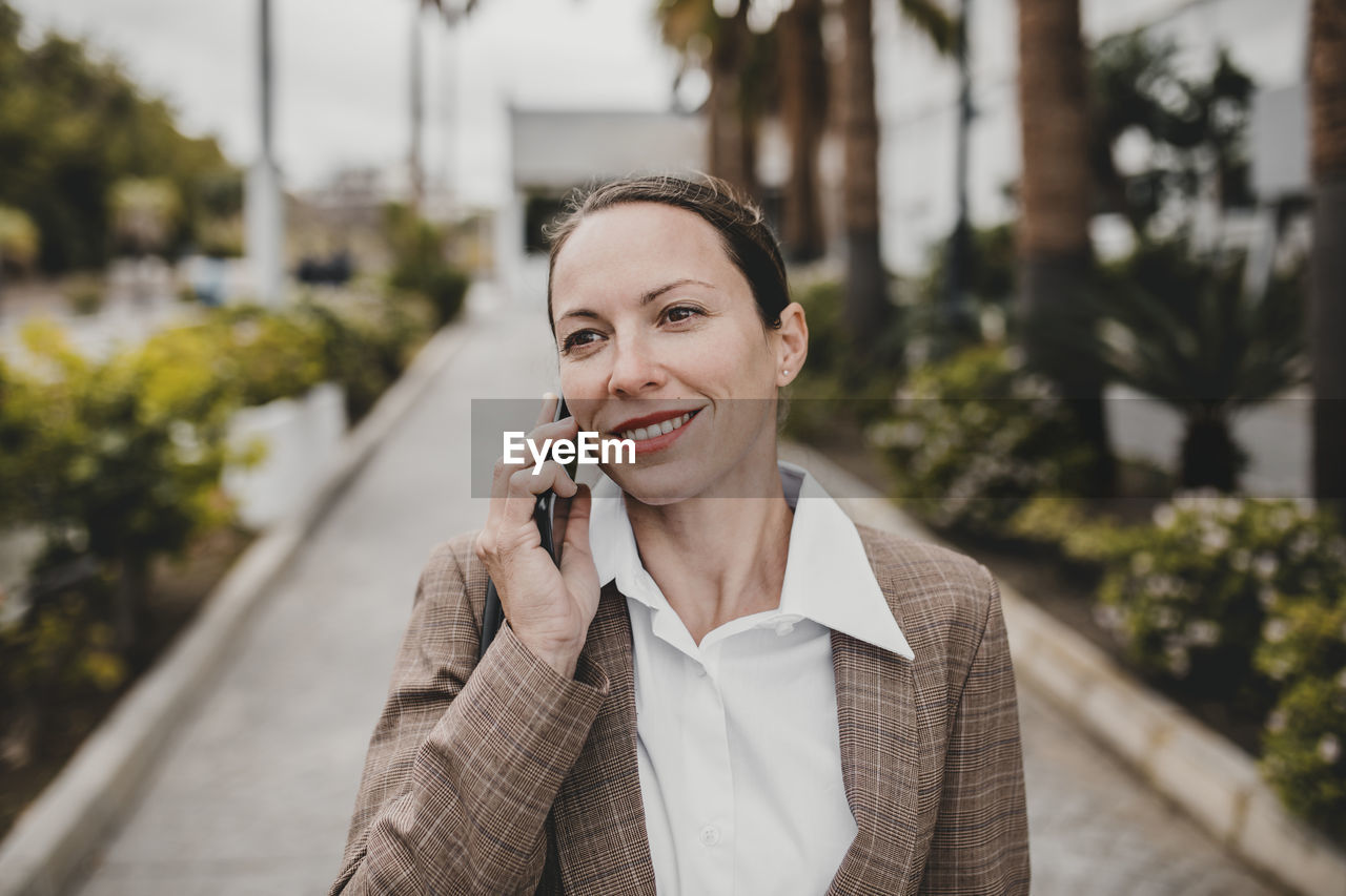Smiling female entrepreneur talking on phone looking away