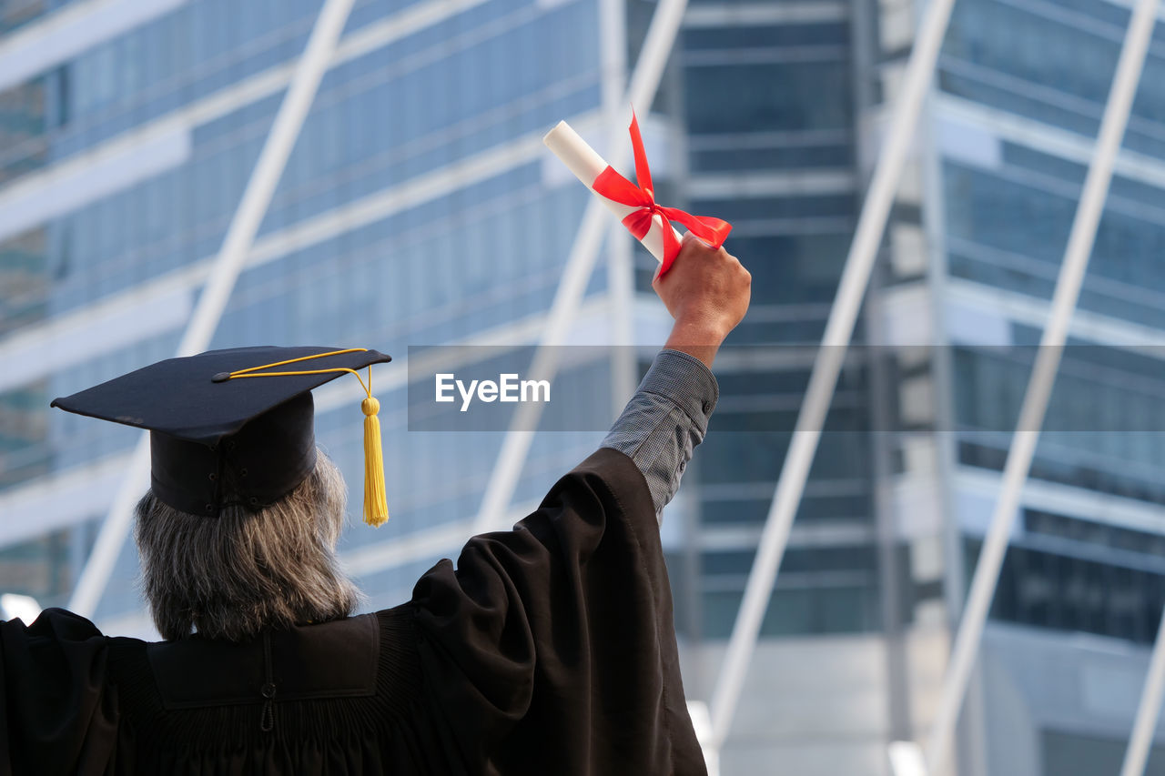 Rear view of man wearing graduation gown against building