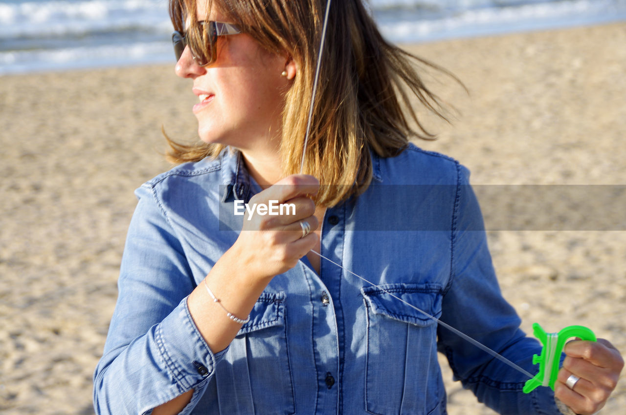 Woman looking away while flying kite at beach