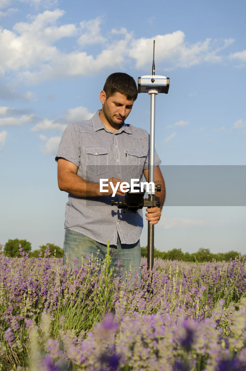 Surveyor with theodolite on lavender field against sky