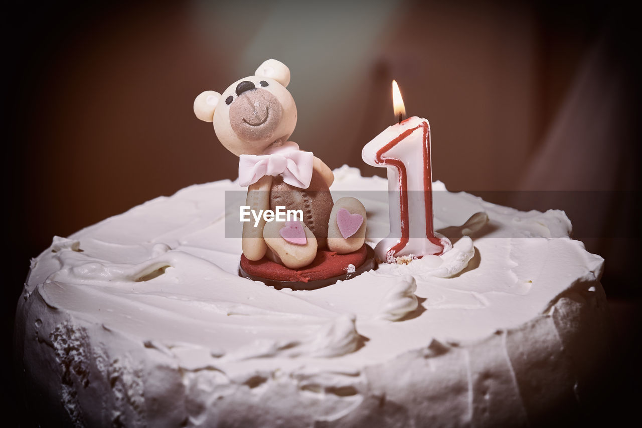 Close-up of burning candle with bear figurine on cake