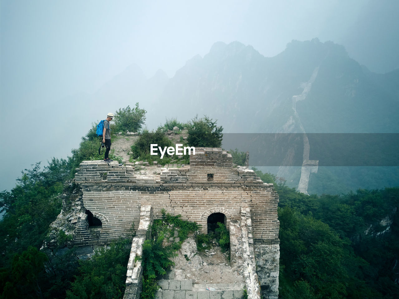 Side view of man standing on old ruin against mountain during foggy weather