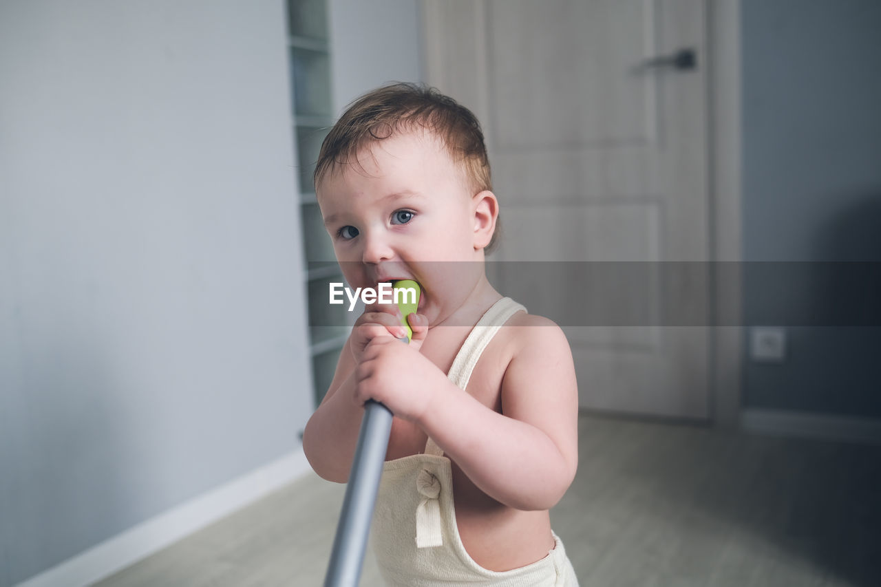 One-year-old child gnaws on handle of mop, cuts teeth and help mother. bright real interior, toning.