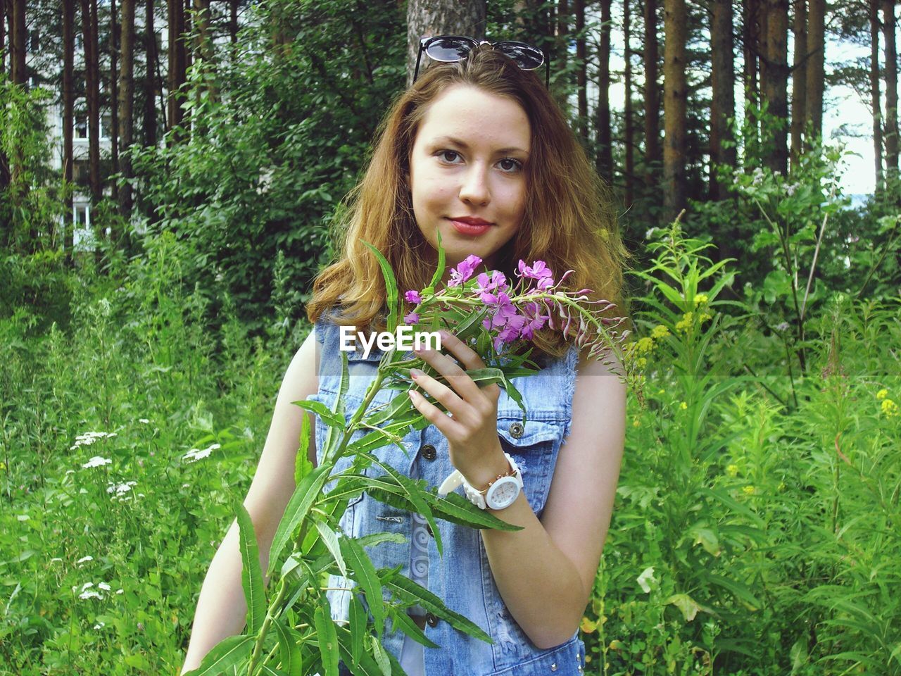 Portrait of young woman touching flowering plant in forest