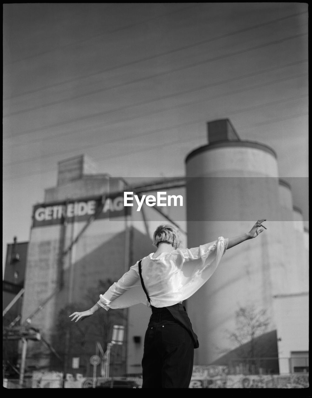 REAR VIEW OF MAN STANDING AGAINST BUILT STRUCTURE