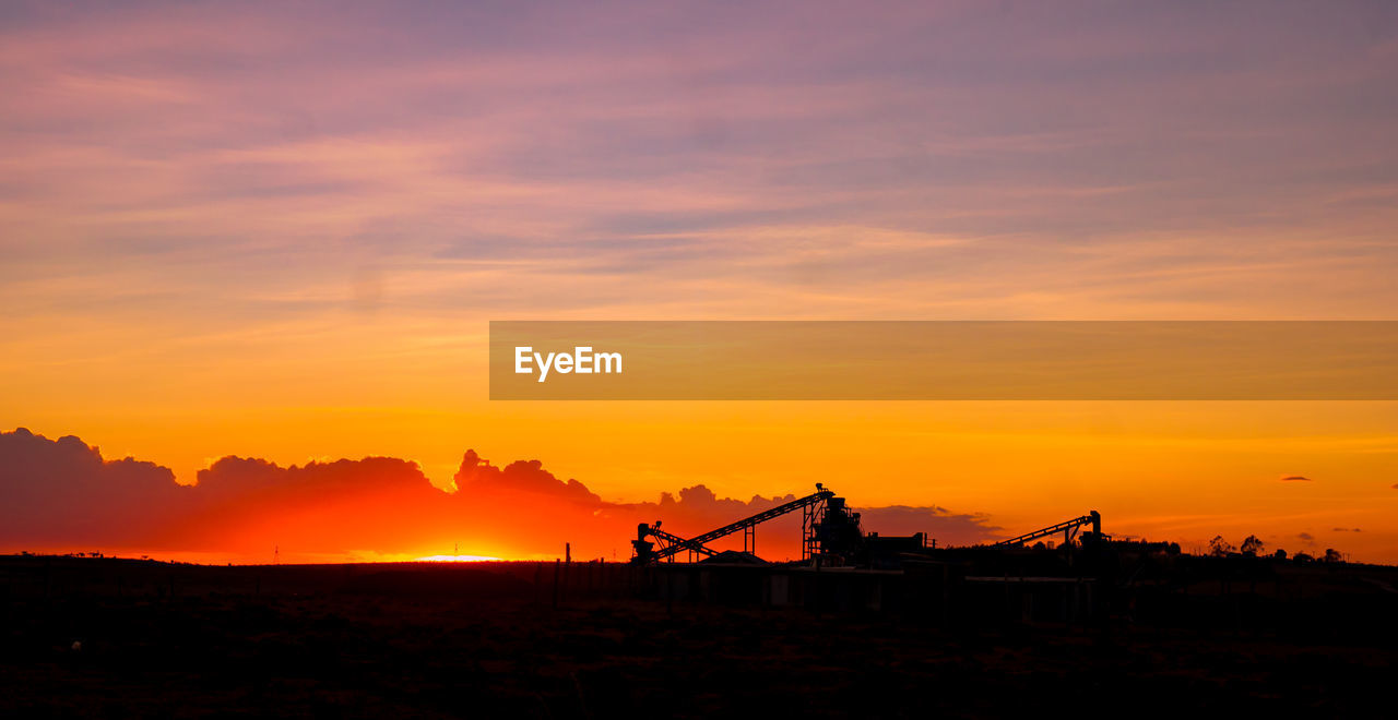 Silhouette cranes at construction site against sky during sunset