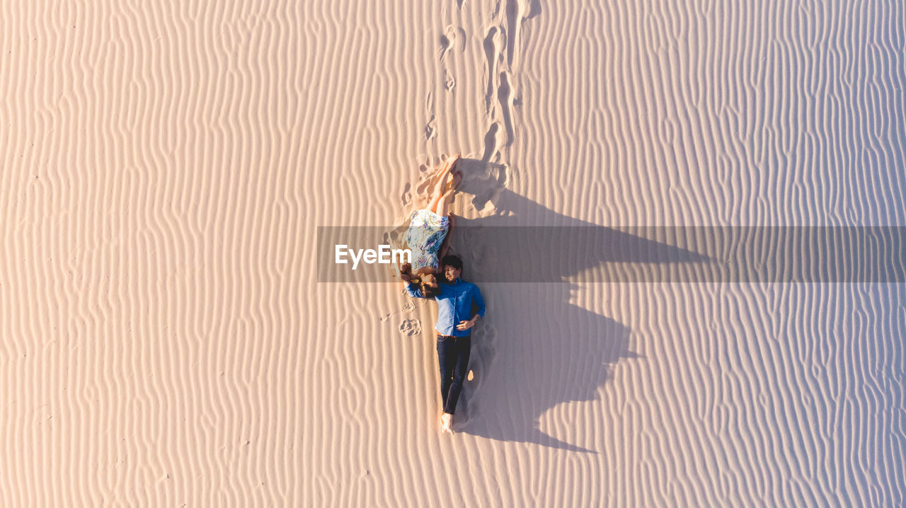 High angle view of couple lying on sand at desert