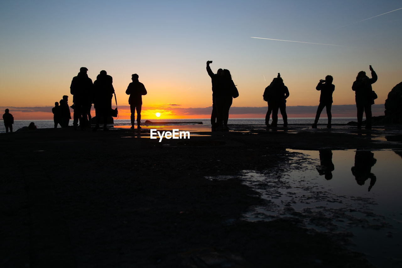 SILHOUETTE PEOPLE AT BEACH AGAINST SKY DURING SUNSET