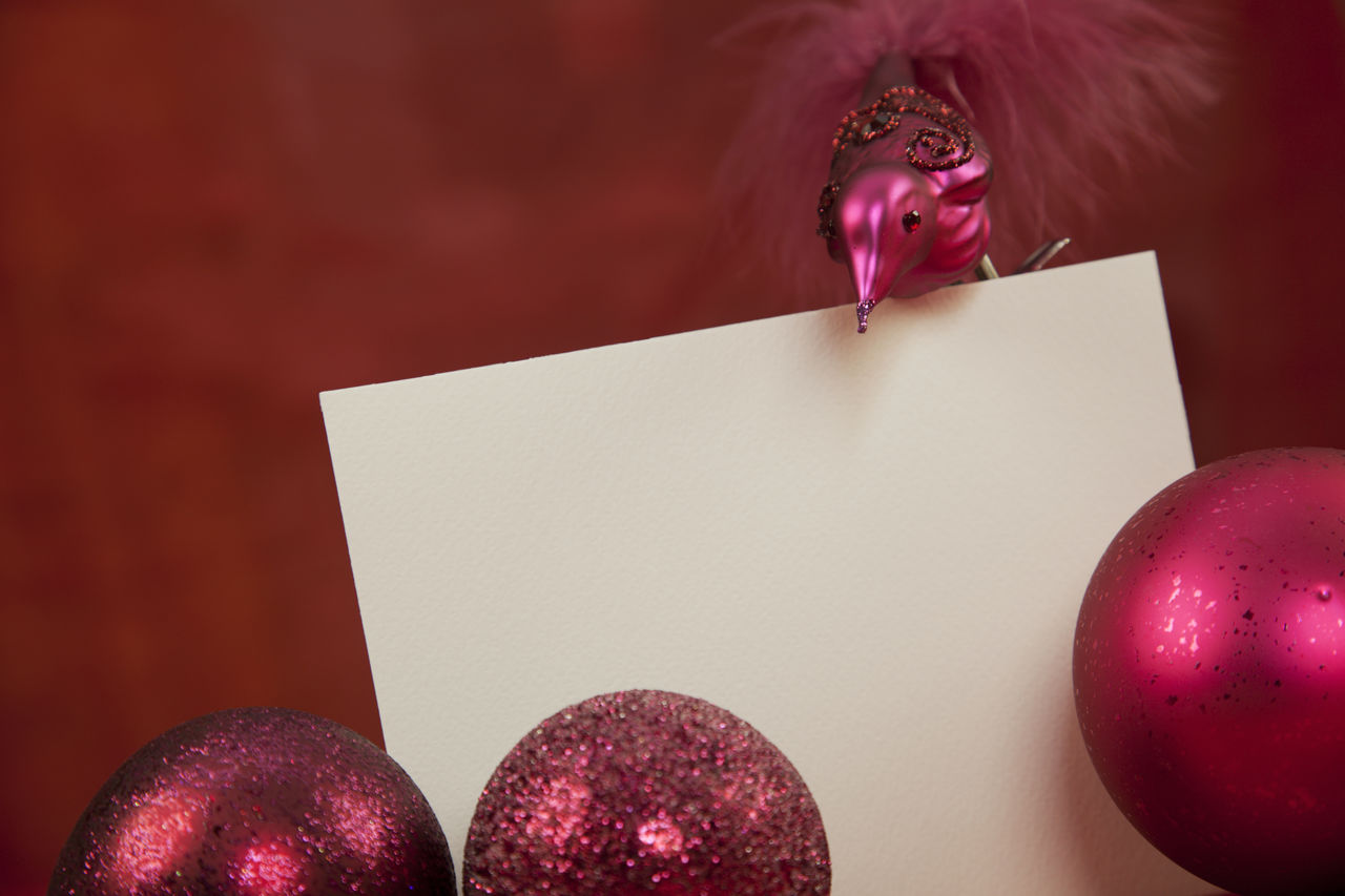 Close-up of placard with pink christmas baubles and figurine against red background