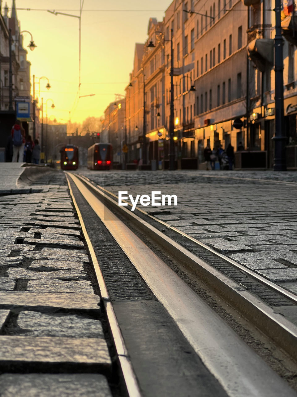 architecture, road, track, street, city, railroad track, urban area, building exterior, transportation, built structure, lane, transport, rail transportation, mode of transportation, cityscape, evening, sky, sunset, vehicle, nature, city life, travel destinations, public transportation, travel, city street, road surface, infrastructure, outdoors, train, building, cable car, walkway, sunlight
