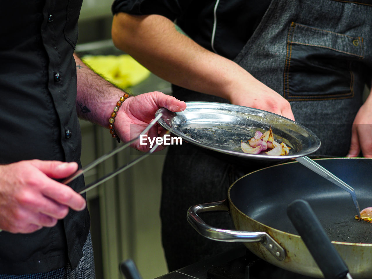 Chef cooking and grilling onions and a golden potato on a pan in a professional restaurant kitchen.